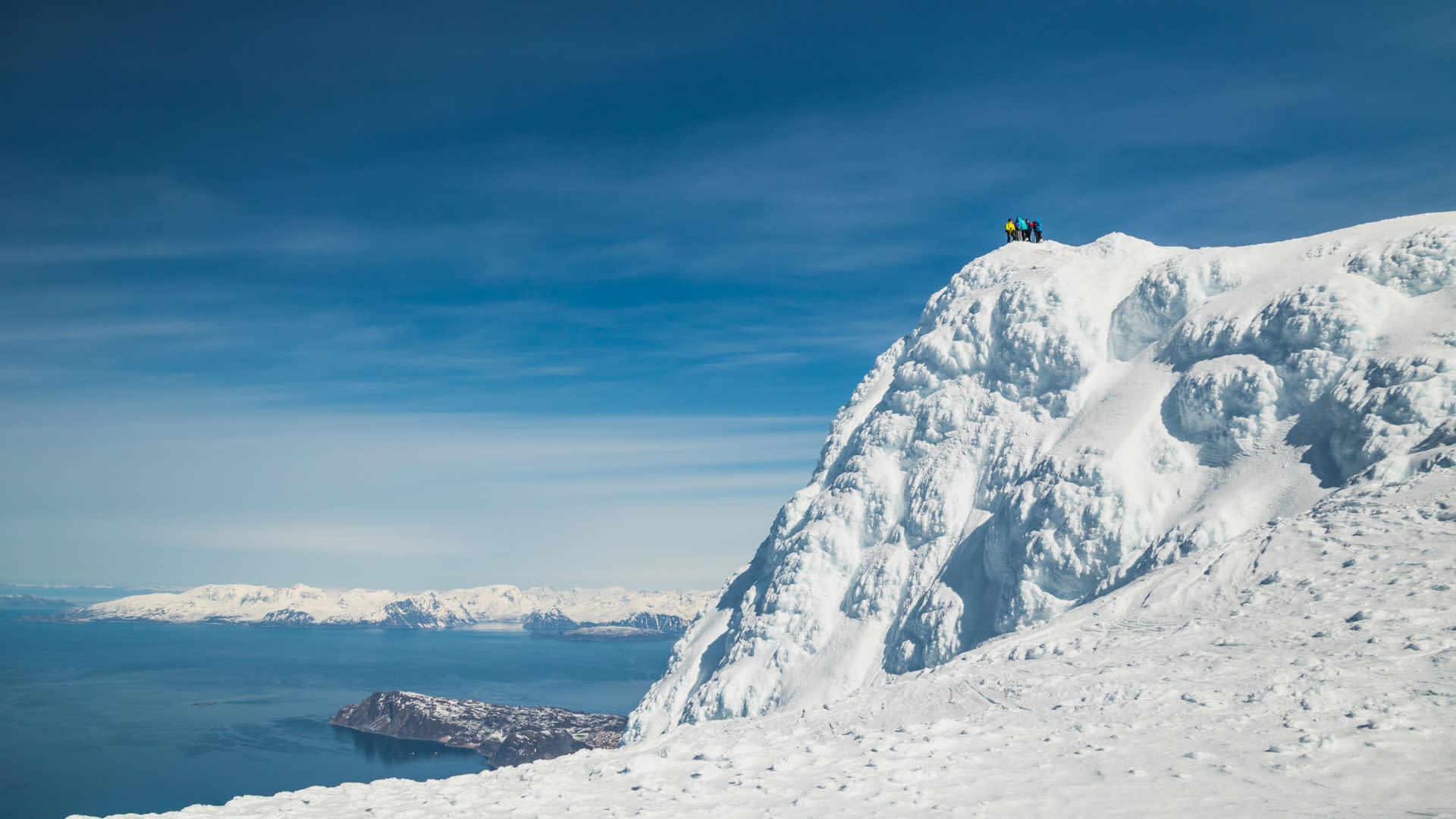 Drei Skitourengeher auf dem Gipfel des Store Kagstinden mit Blick auf Fjord und Berge der Lyngen Alps.
