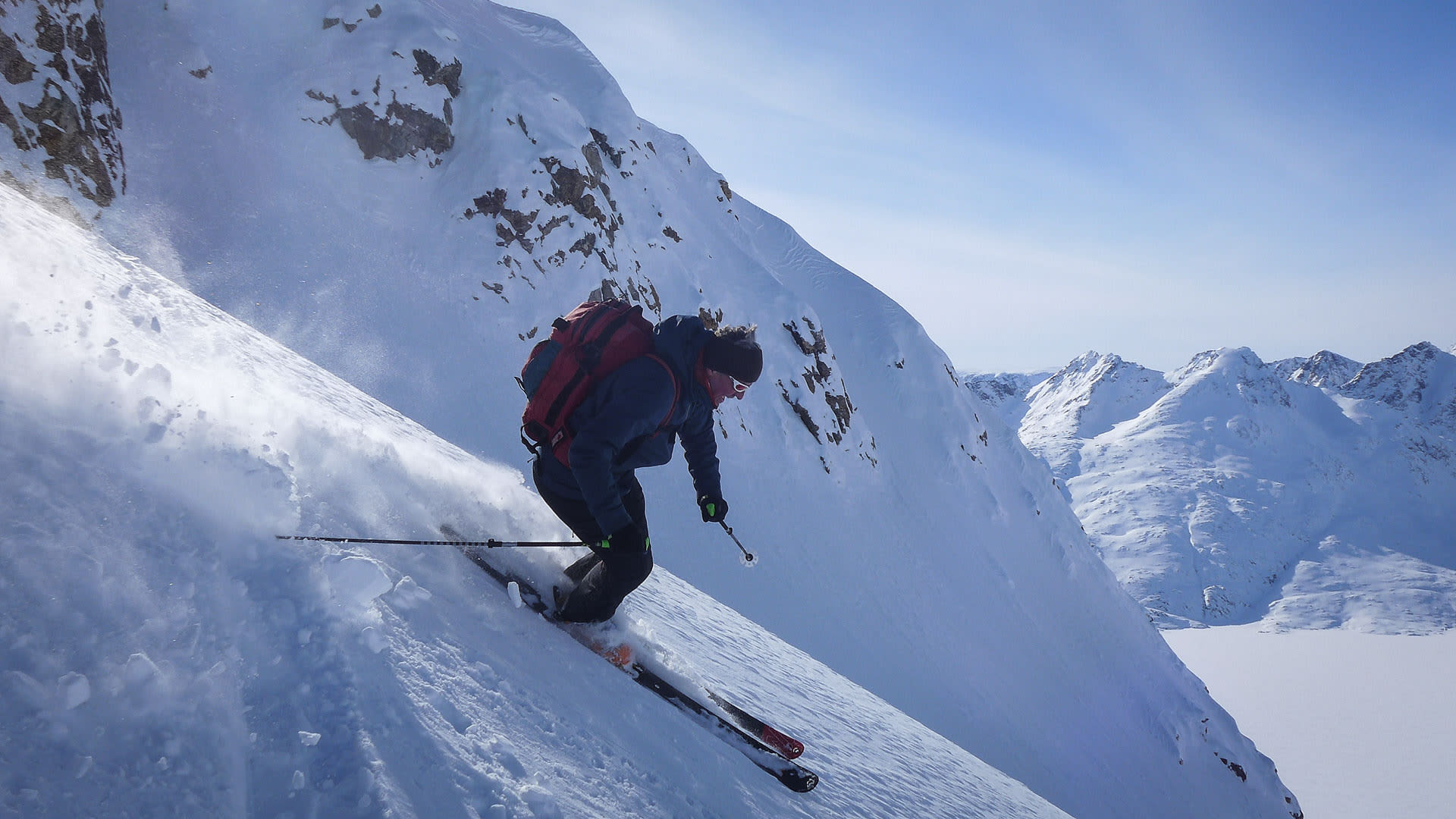 Person auf Skitour bei Tasiilaq in Grönland fährt steilen Tiefschnee-Hang ab, aufgewirbeltes Schneepulver