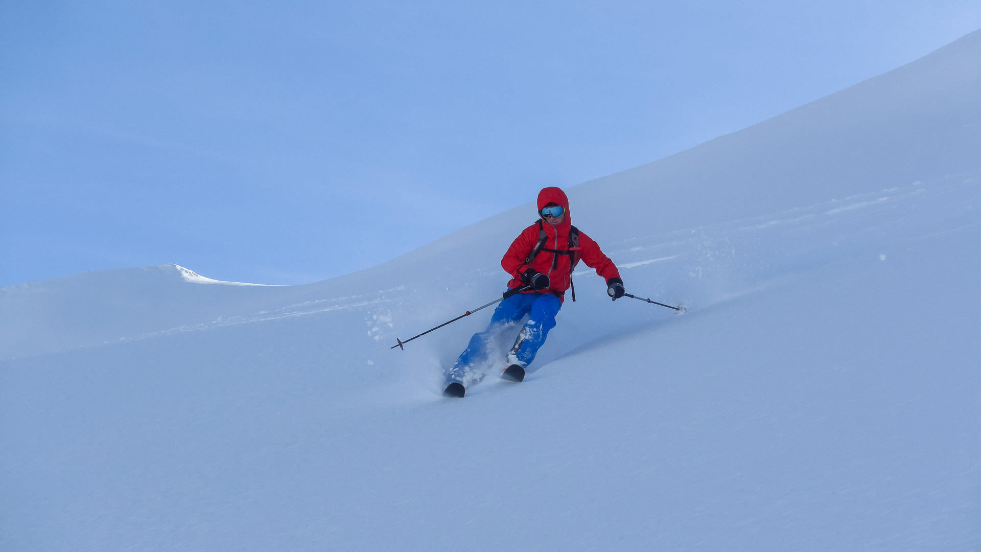 Skitourengeher in roter Jacke fährt einen unverspurten Tiefschnee-Hang in Swanetien ab, hinter den Skiern eine Schneestaubwolke.