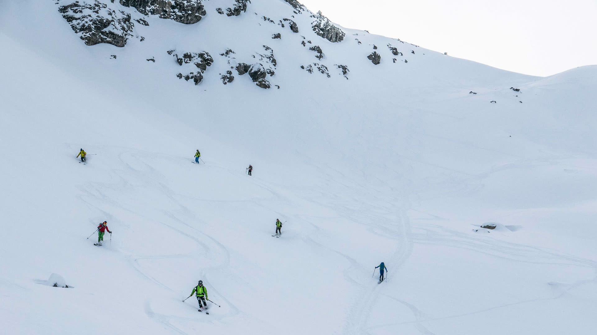 Sieben Skitourengeher fahren im Tiefschnee den Steilhang im Schafkar im Lechtal ab.