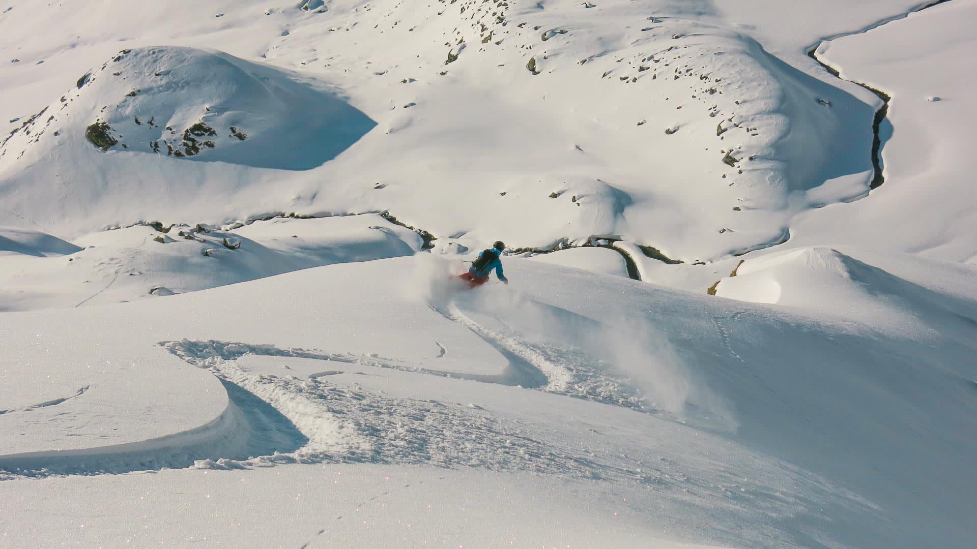 Freerider in türkisfarbener Jacke fährt durch Pulverschnee auf unverspurtem Hang in der Gotthardgruppe.