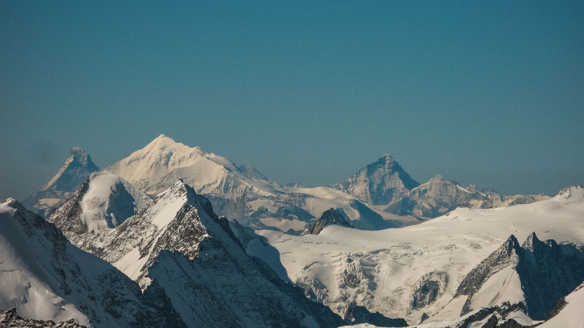 Skitour Berner Oberland: Weisshorn mit pyramidalem Gipfel über Gletscherplateau und verschneiten Felszinken im Vordergrund.