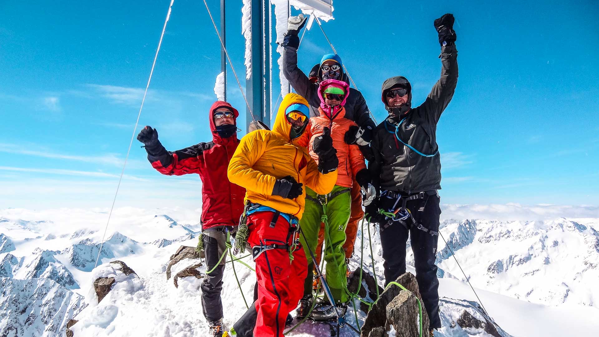 Fünf Skitourengeher posieren am eisbedeckten Gipfelkreuz der Wildspitze auf der Venter Runde mit weitem Hochgebirgspanorama.