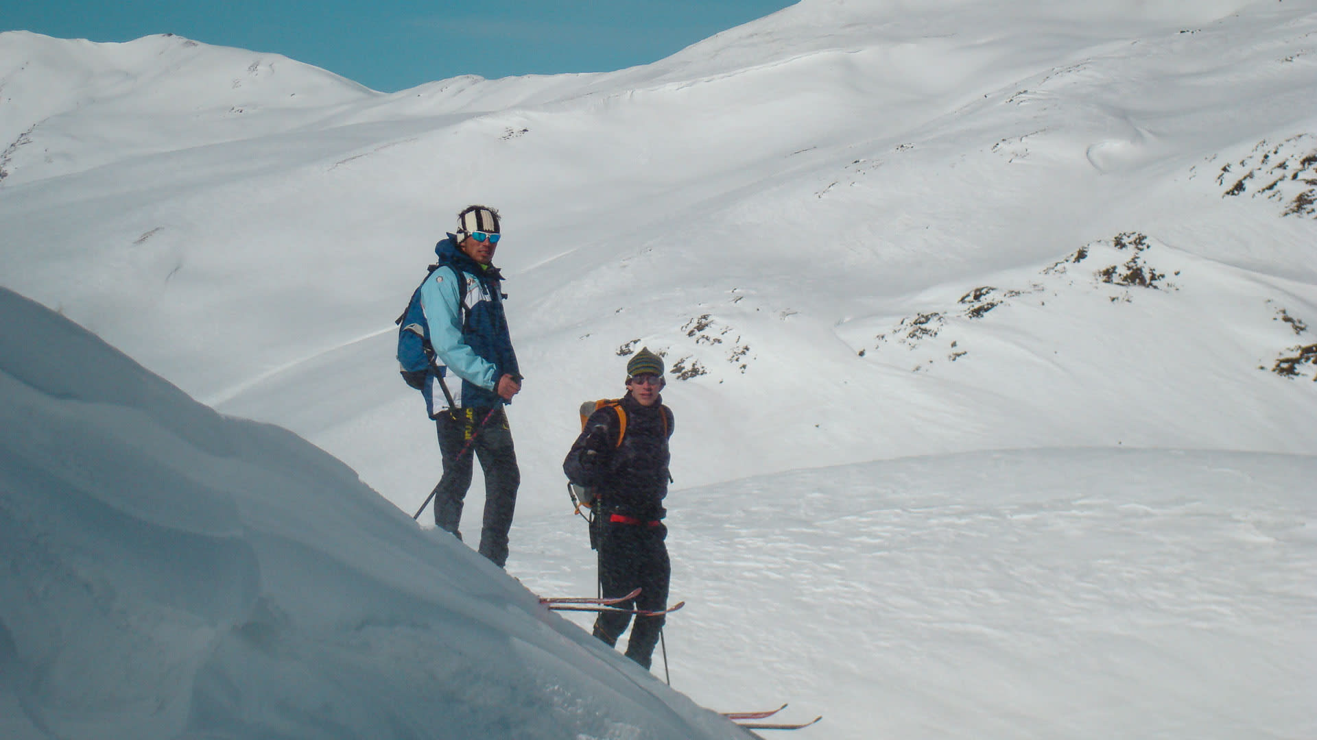 Zwei Skitourengeher mit Tourenski und Fellen stehen auf einem sonnigen Schneehang bei der Sesvennahütte in Südtirol.