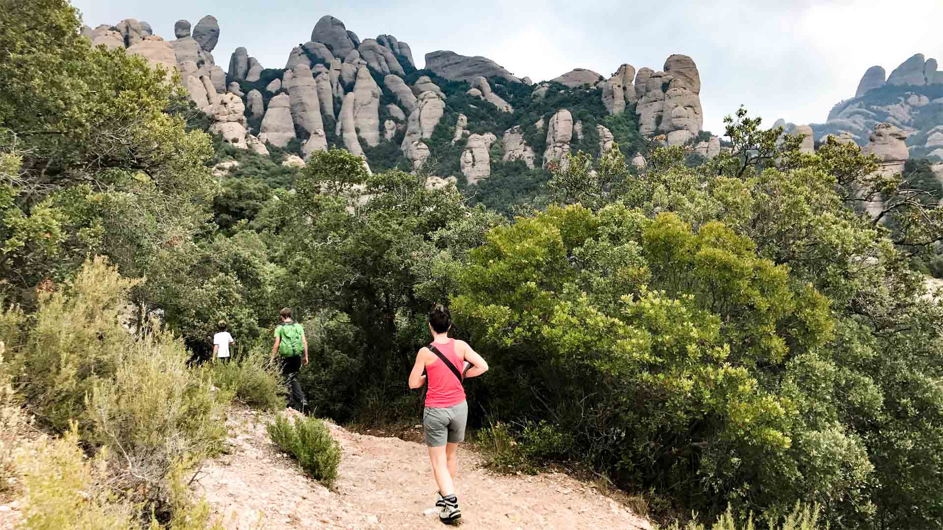Trekking am Montserrat: drei Trekker steigen auf sandig-felsigem Pfad durch Macchie auf, dahinter säulenartige