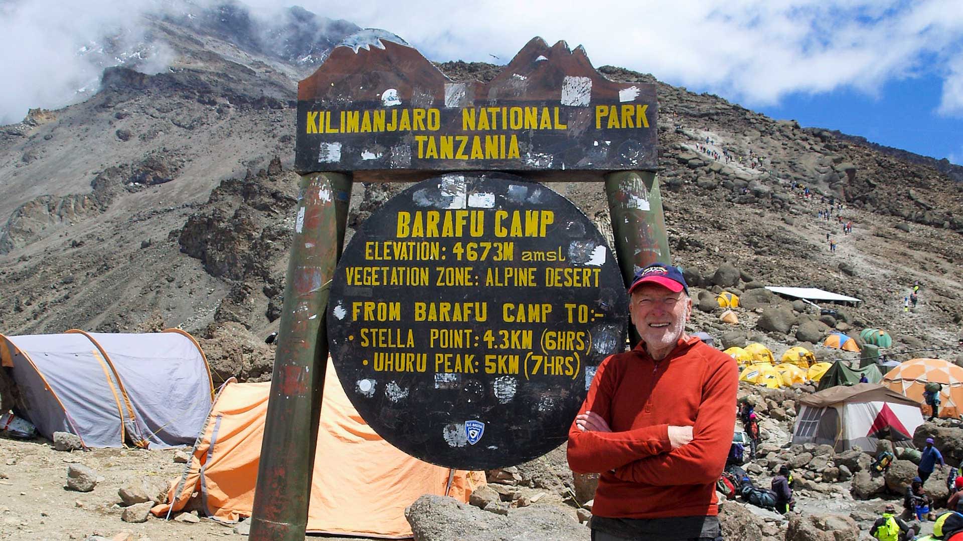 Trekker steht vor dem Barafu-Camp-Schild auf 4673 m im Kilimandscharo-Nationalpark mit Zeltlager und Aufstiegshang.