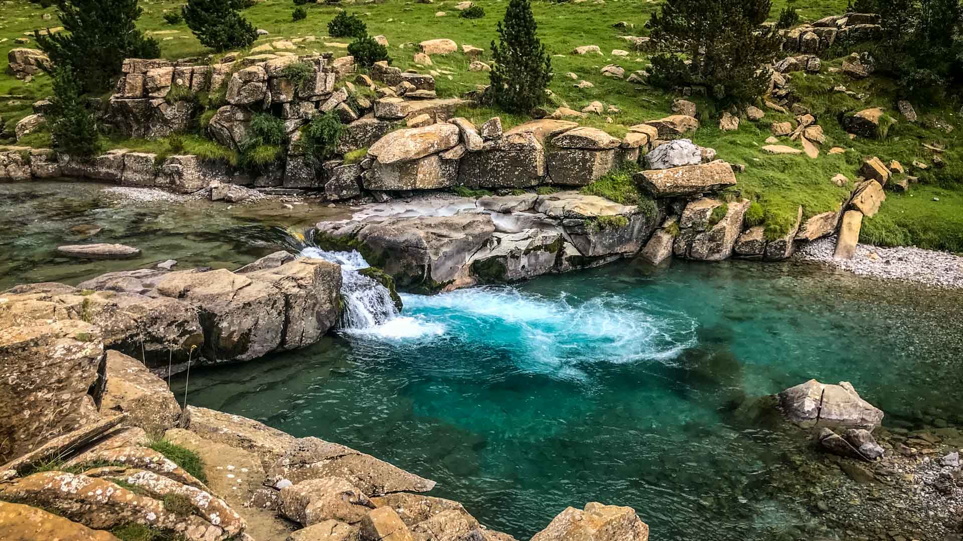Türkisfarbener Gebirgsbach mit kleinem Wasserfall über Granitsteine auf einem Hochplateau der Pyrenäen.