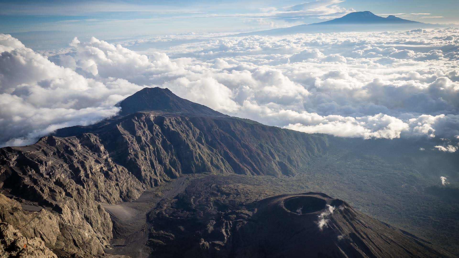 Trekking am Mount Meru: Luftperspektive auf Vulkankrater mit Blick auf den Kilimandscharo über geschlossener Wolkendecke
