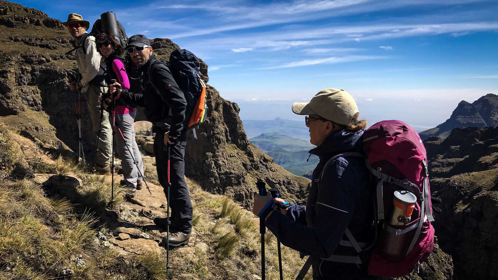 Wandergruppe beim Trekking in den Drakensbergen: vier Personen mit Großrucksäcken und Trekkingstöcken auf felsigem Plateau