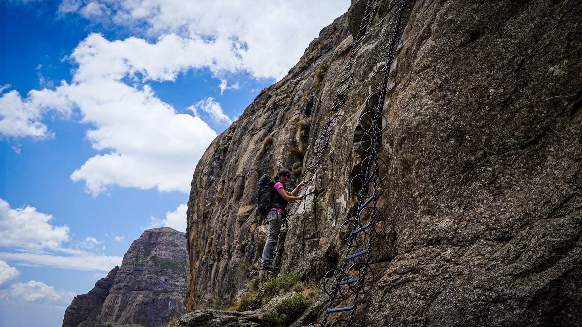 Trekking in den Drakensbergen: Person klettert an einer vertikal montierten Metallkette mit ringförmigen Griffen die Eisenleitern