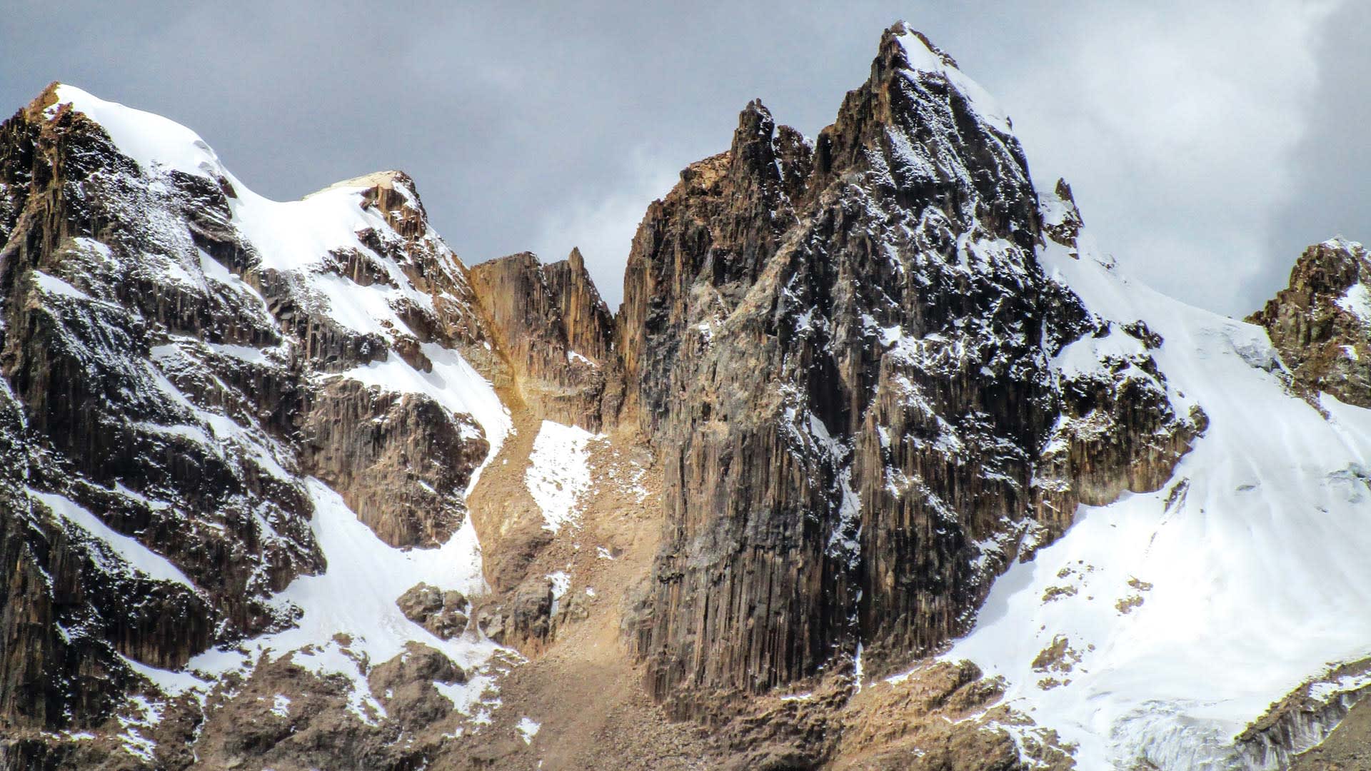Trekking im Huayhuash: steil aufragende Felsformationen am Cacananpunta Hochpass mit Schnee- und Eisauflagerungen.