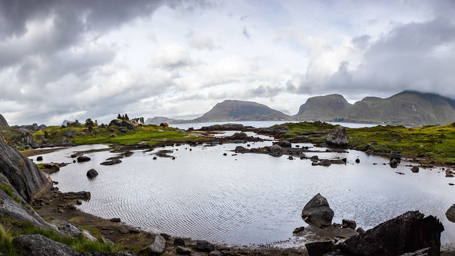 Trekking auf den Lofoten: Küstenlandschaft mit Gezeitenbecken, roten und weißen Gebäuden sowie steil aufragenden Bergmassiven