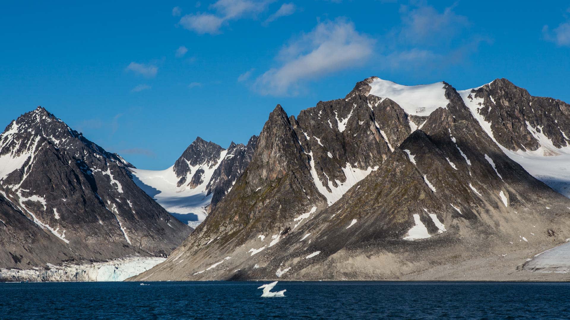 Trekking auf Spitzbergen: Gletscherkalbungsfront mit türkisblauem Eis im arktischen Fjord, zerklüftete Felsgipfel im Hintergrund.