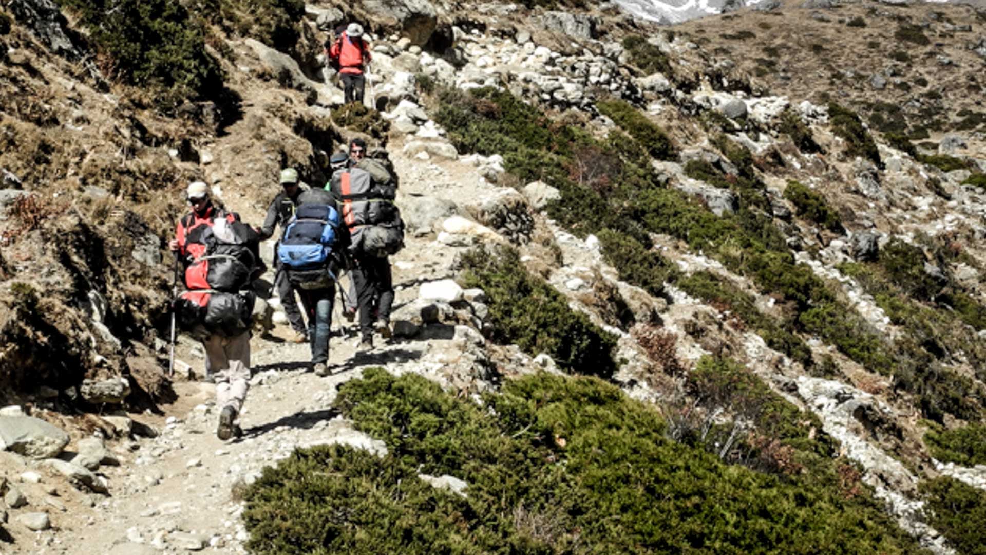 Gokyo Trek Nepal: Trekking-Gruppe mit vollbepackten Rucksäcken steigt auf steinigem Pfad durch felsiges Gelände im Khumbu-Himalaya