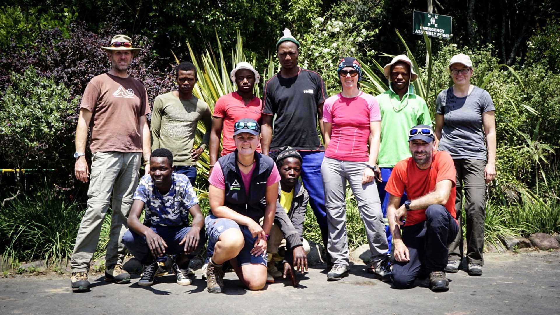 Gruppenfoto von elf Trekking-Teilnehmern in zwei Reihen vor tropischer Vegetation im Maloti-Drakensberg Park, Südafrika