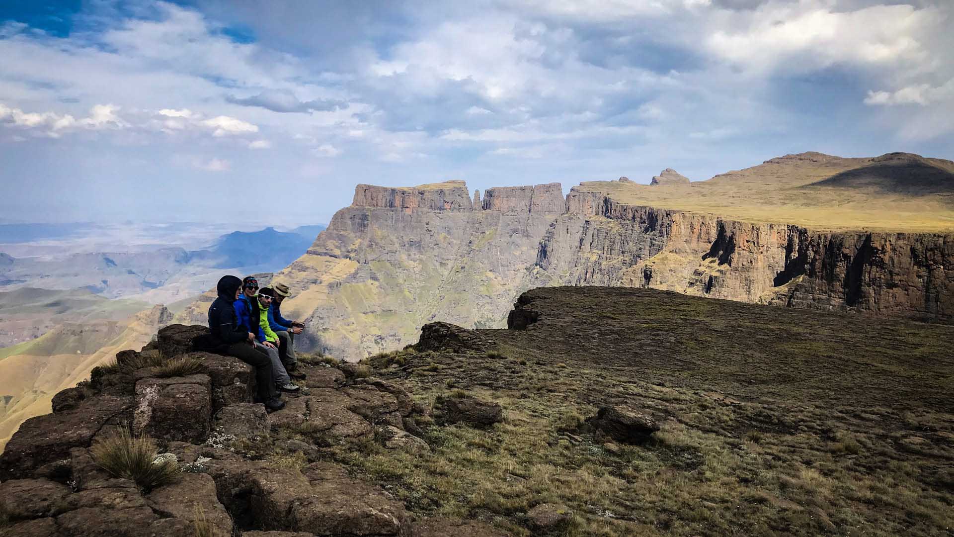 Drei Trekker rasten auf einem Felsvorsprung mit Blick auf die Basaltsteilwände der Tugela Falls in den Drakensbergen.