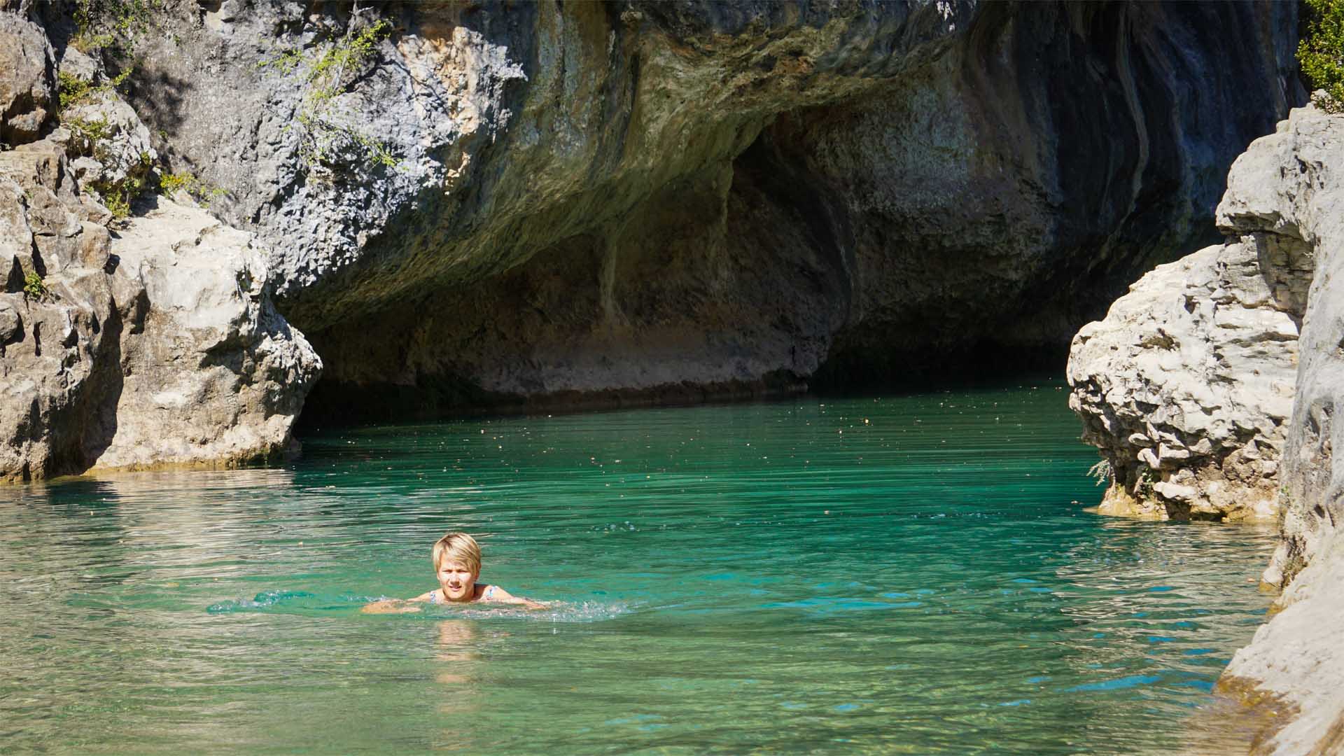 Trekking bei Rodellar: Person schwimmt im türkis-grünen Naturbecken des Alcanadre, umgeben von hellem Kalkgestein und Felsüberhang