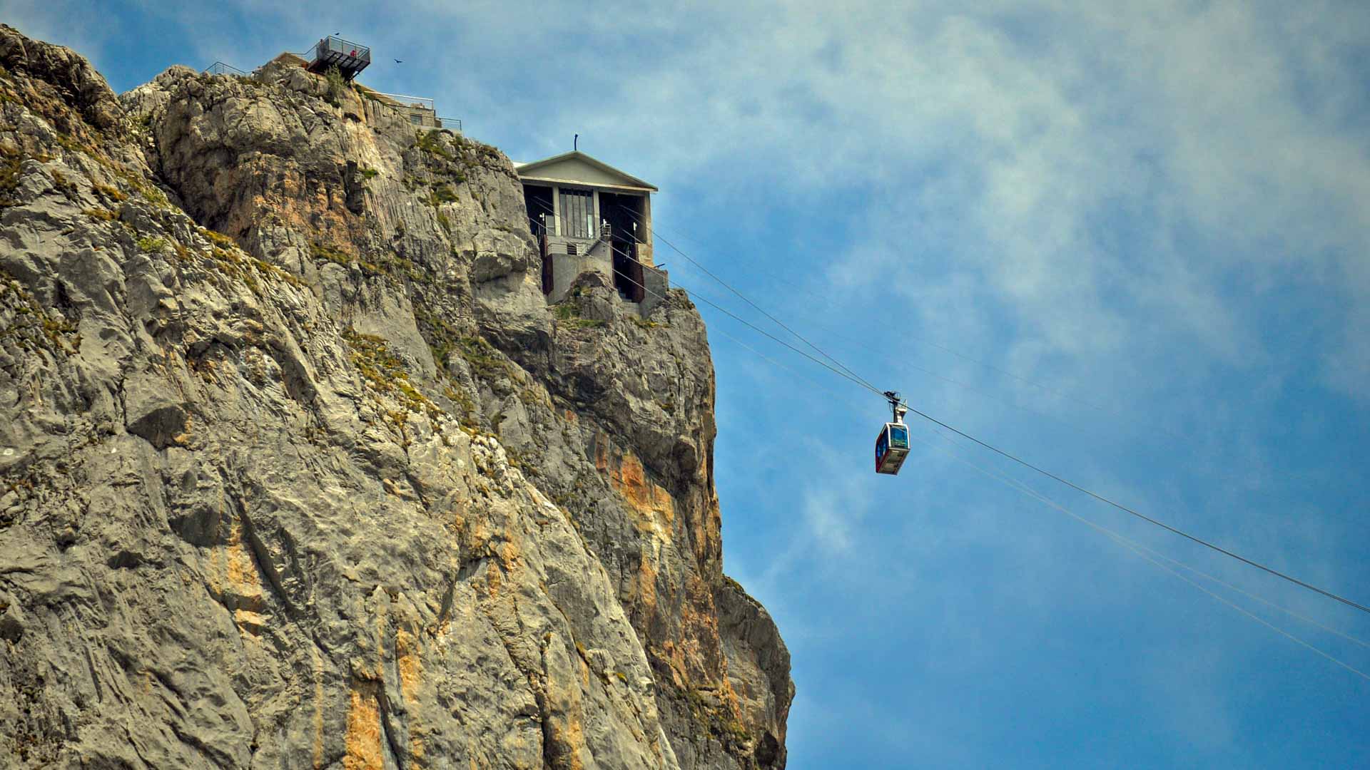 Trekking Picos de Europa: Seilbahnkabine der Fuente Dé hängt vor steil aufragender Kalkfelswand mit Bergstation.