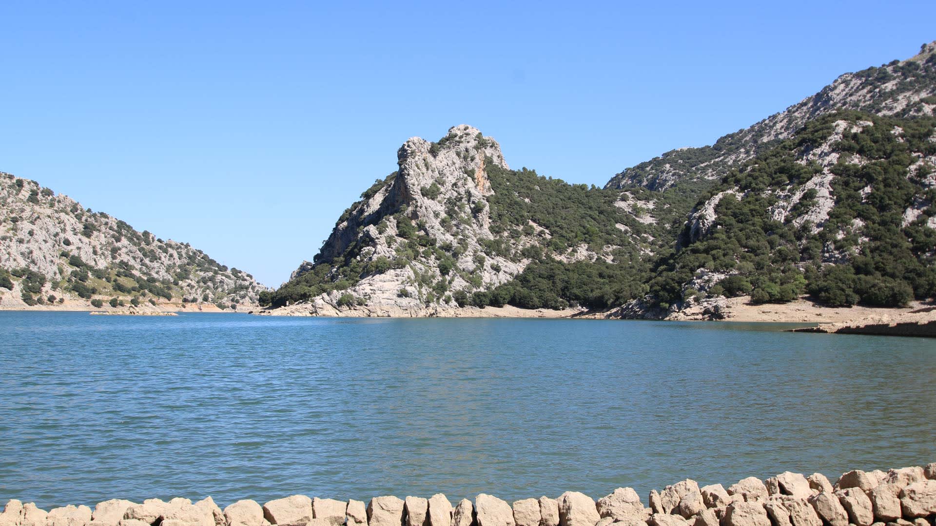 Trekking in der Serra de Tramuntana: Stausee mit blau-grünem Wasser, Kalksteindamm und bewaldeten Berghängen.