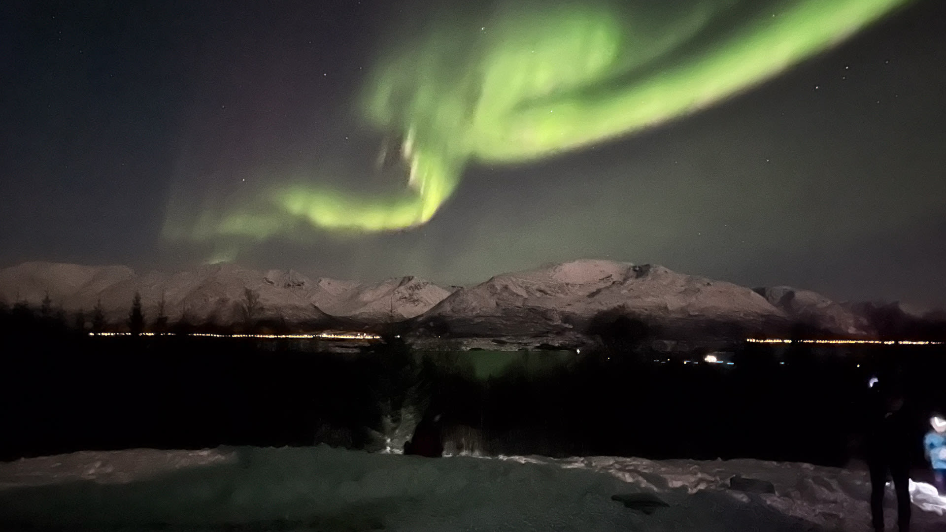 Winterwanderung in Norwegen: Drei Winterwanderer beobachten gelbgrüne Polarlichter über verschneiten Bergen bei Nacht.