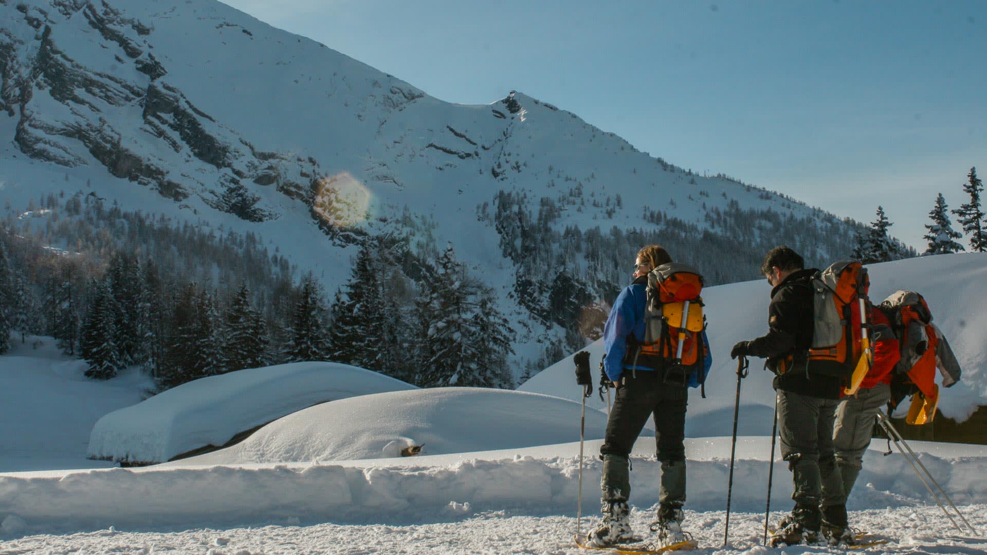 Zwei Winterwanderer mit Schneeschuhen und Rucksäcken blicken auf einen schneebedeckten Felsgipfel in Berchtesgaden.