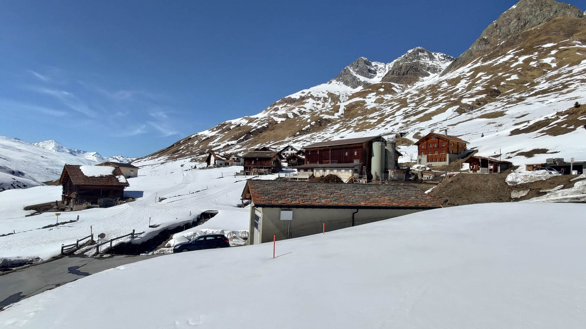 Winterwanderung in Juf im Averstal: alpine Bergsiedlung mit Holzgebäuden, Markierungsstangen im Schnee und steilem Felsberggipfel.