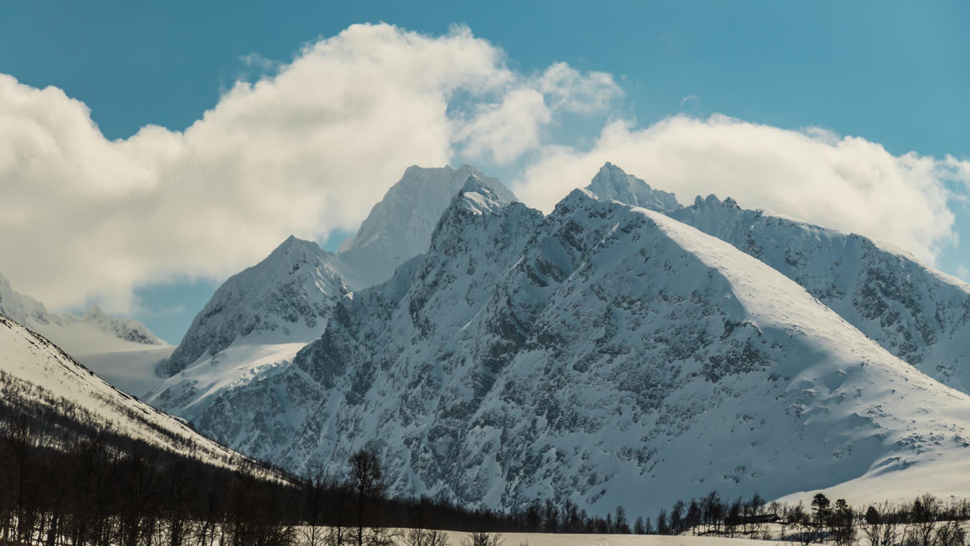Felsige, schneebedeckte Gipfel des Skitourengebiets Lyngenlapen mit verschneitem Talboden im Vordergrund.