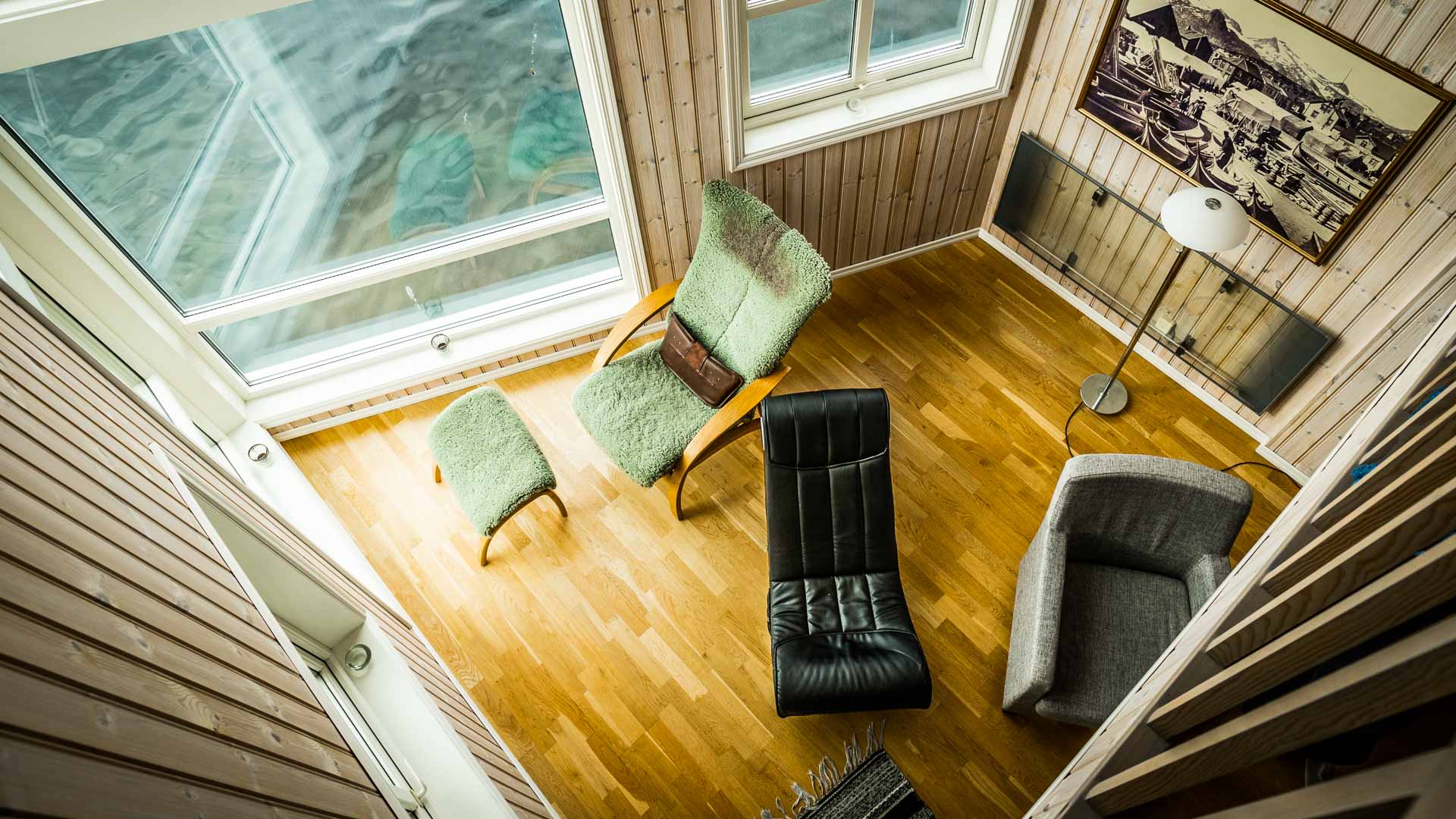 Skitour Lofoten – Wohnbereich im Svinøya Rorbu mit Holzpaneelen, Retro-Sesseln und Fjordblick durch große Fenster.