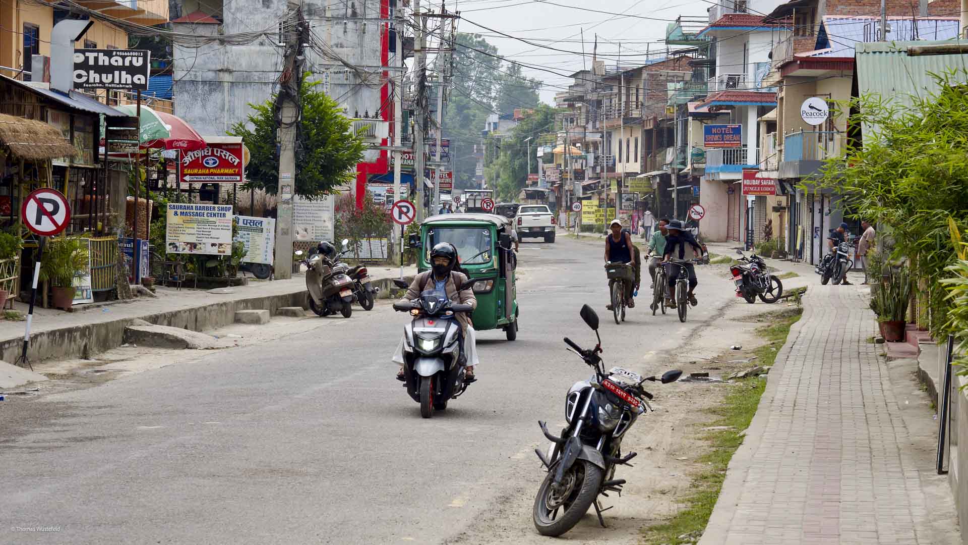 Trekking-Basis Sauraha in Chitwan, Südnepal: belebte Hauptstraße mit Motorrollern, Rikschas und Läden in Devanagari-Schrift.
