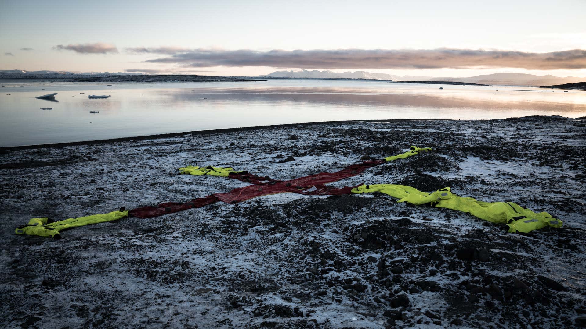 Rotes X-Kreuz mit neongelben Survival-Suits als Suchmarkierung an arktischer Küste im Winter.