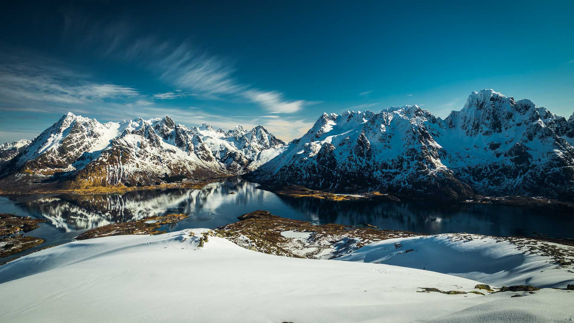 Skitour auf den Lofoten: verschneiter Hang mit Blick auf Fjord und Bergkette im Winter.