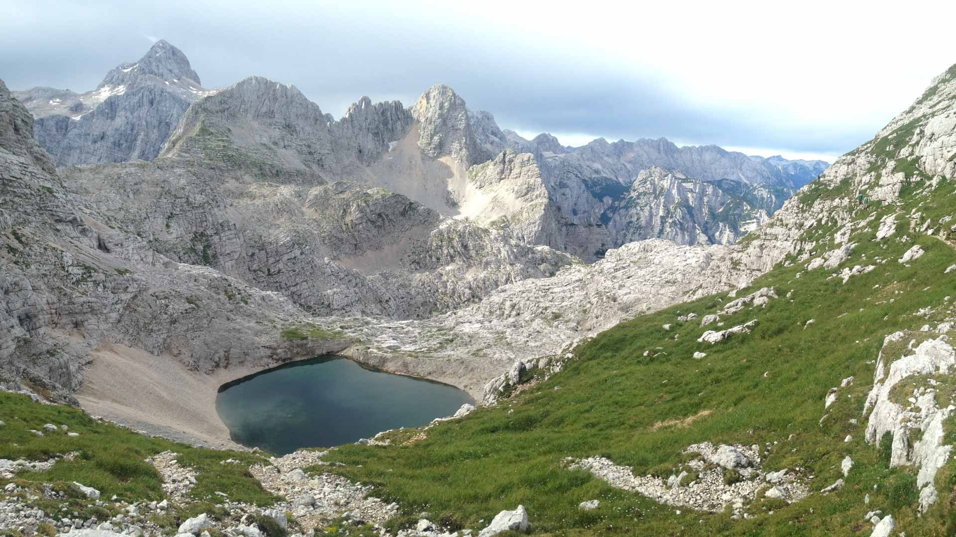 Bergtour in den slowenischen Bergen: Hochgebirgssee in einem Kalksteinkar mit Felsgipfeln im Hintergrund.