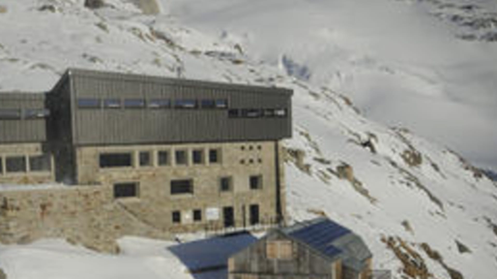 Luftaufnahme des Refuge Albert 1er umgeben von verschneiten Berghängen und Felswänden im Hochgebirge.
