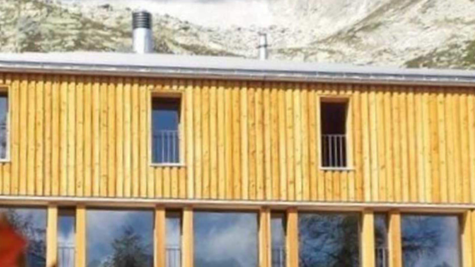 Die Capanna Piansecco präsentiert sich mit gelber Holzfassade und großer Panoramaverglasung im Erdgeschoss.