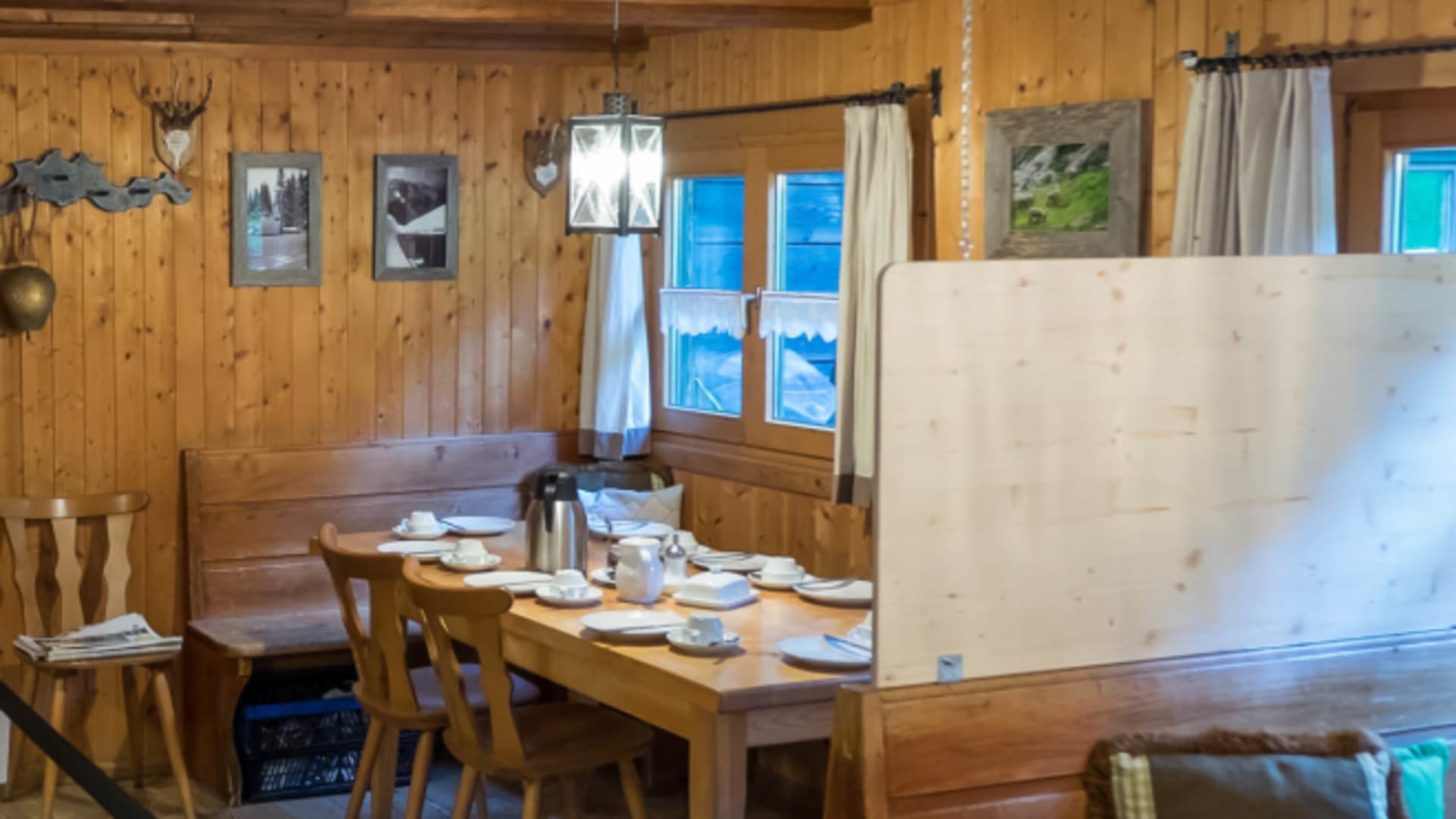 Gastraum der Kenzenhütte mit gedecktem Holztisch und Bergblick durch die Fenster.
