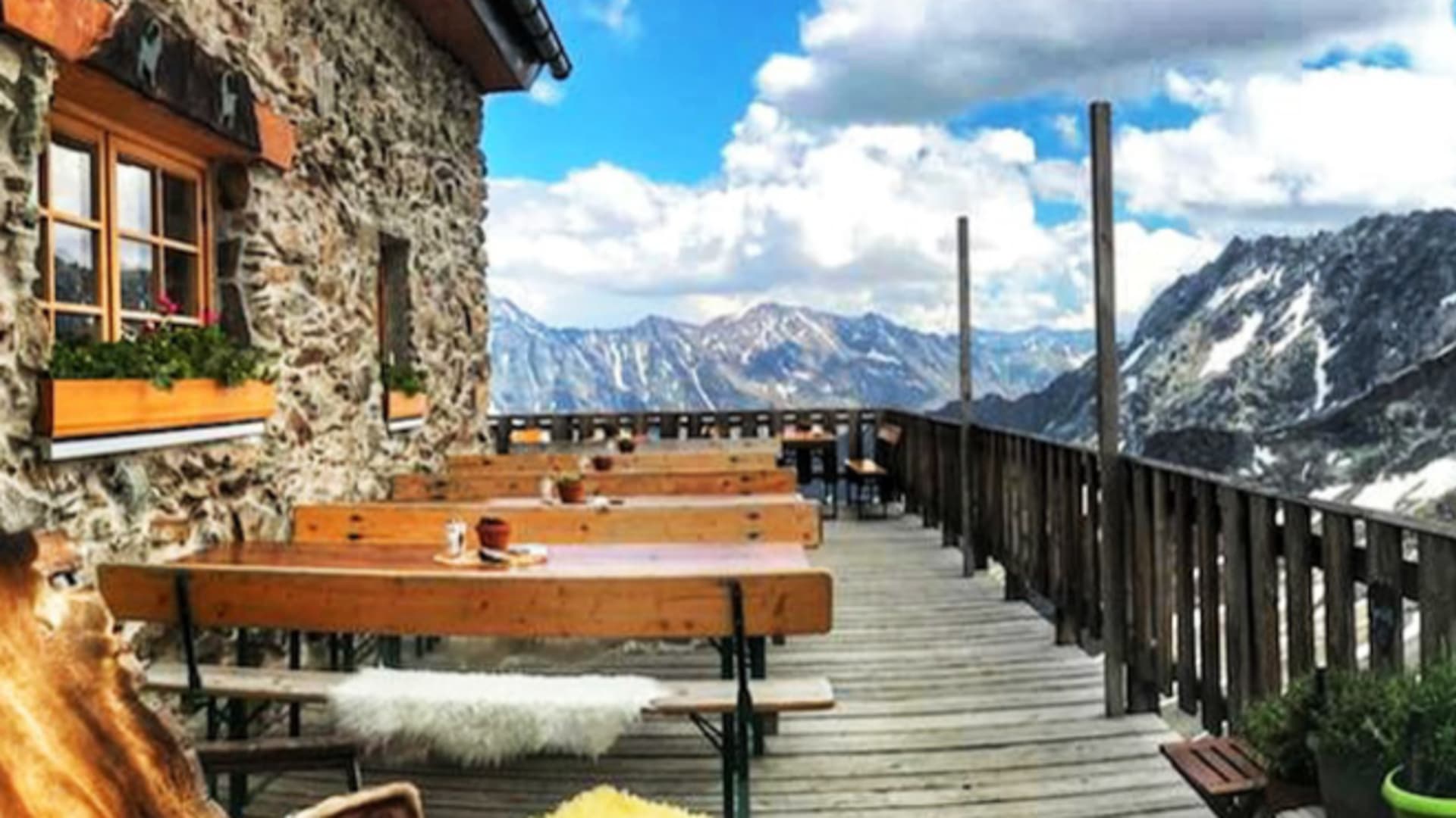 Terrasse der Kaunergrathütte mit geschnitzten Holzmöbeln und Blumenschmuck vor Bergkulisse.