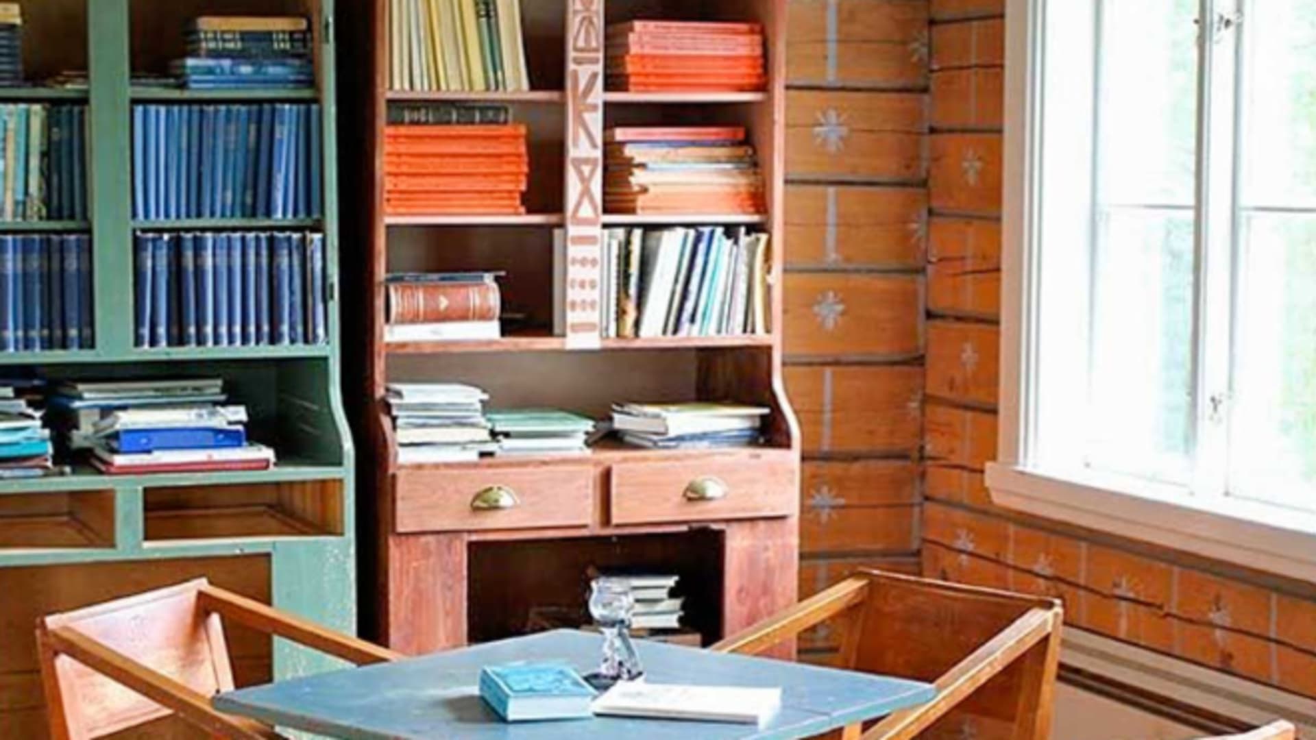 Der Aufenthaltsraum der STF Kvikkjokk Fjällstation zeigt rustikale Holzausstattung mit blauem Tisch und Bücherregalen.