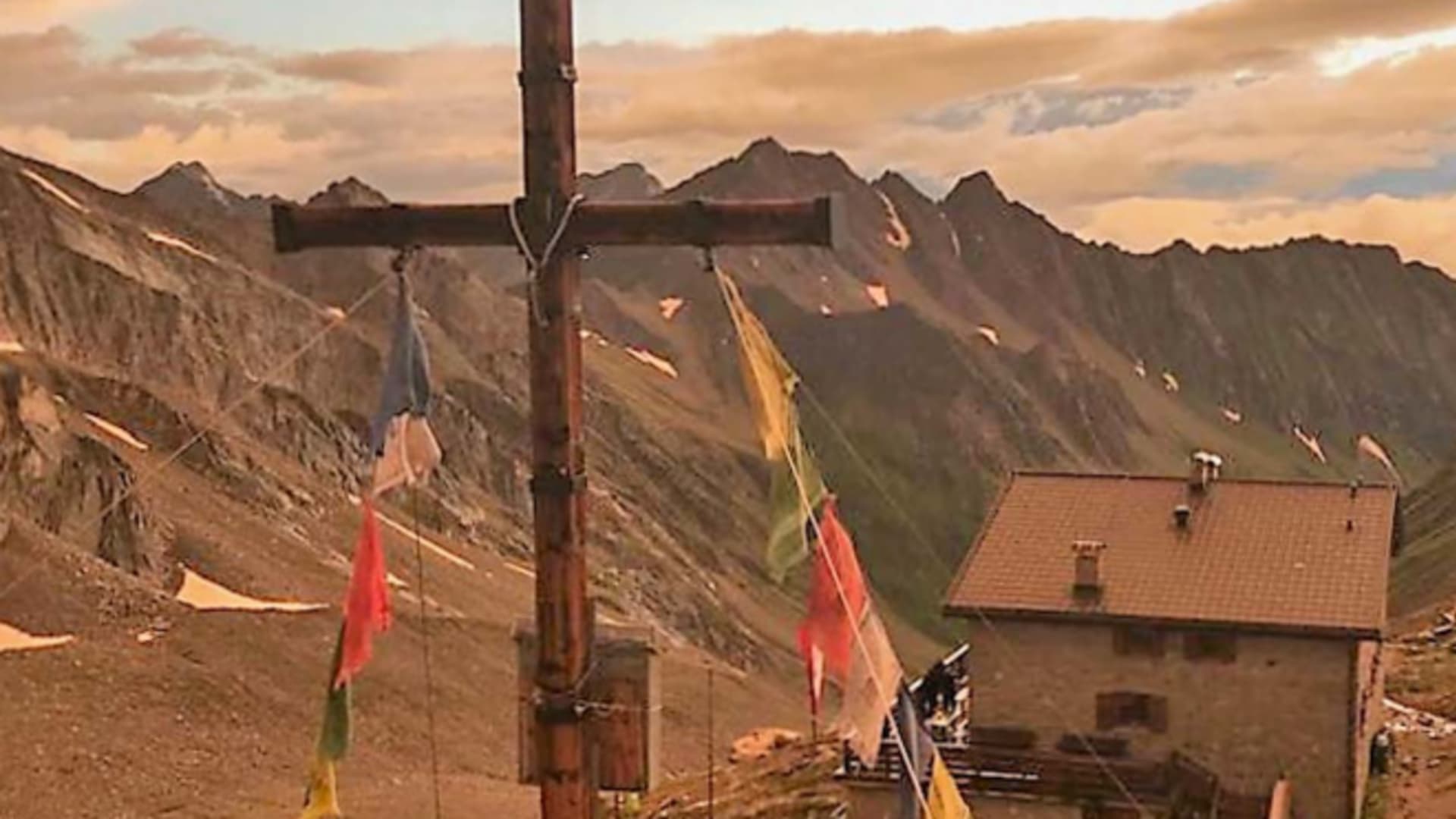 Holzkreuz mit bunten Gebetsfahnen vor der Hochfeilerhütte in hochalpiner Lage während der Abendstunden.