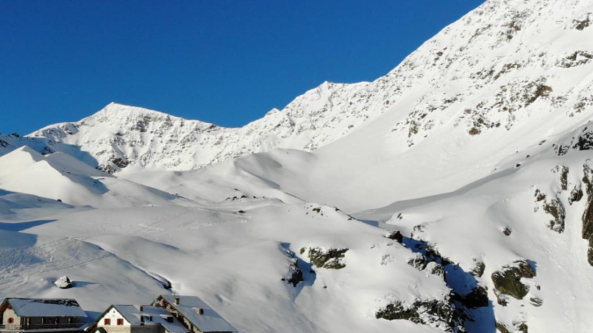 Winterpanorama des Rifugio Branca im verschneiten Hochtal mit umgebenden Bergen und Seilbahninfrastruktur im Ortlergebiet.