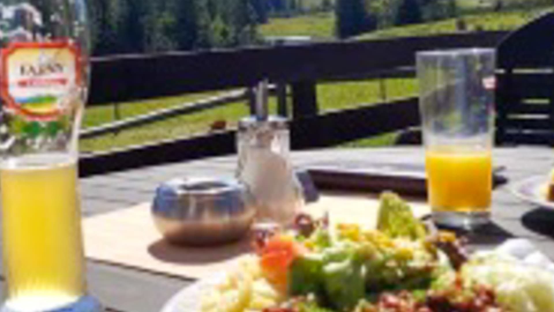Terrasse des Alpengasthof Hörmoos mit gedecktem Holztisch, regionalen Gerichten und Blick auf grüne Wiesen und bewaldete Hügel.