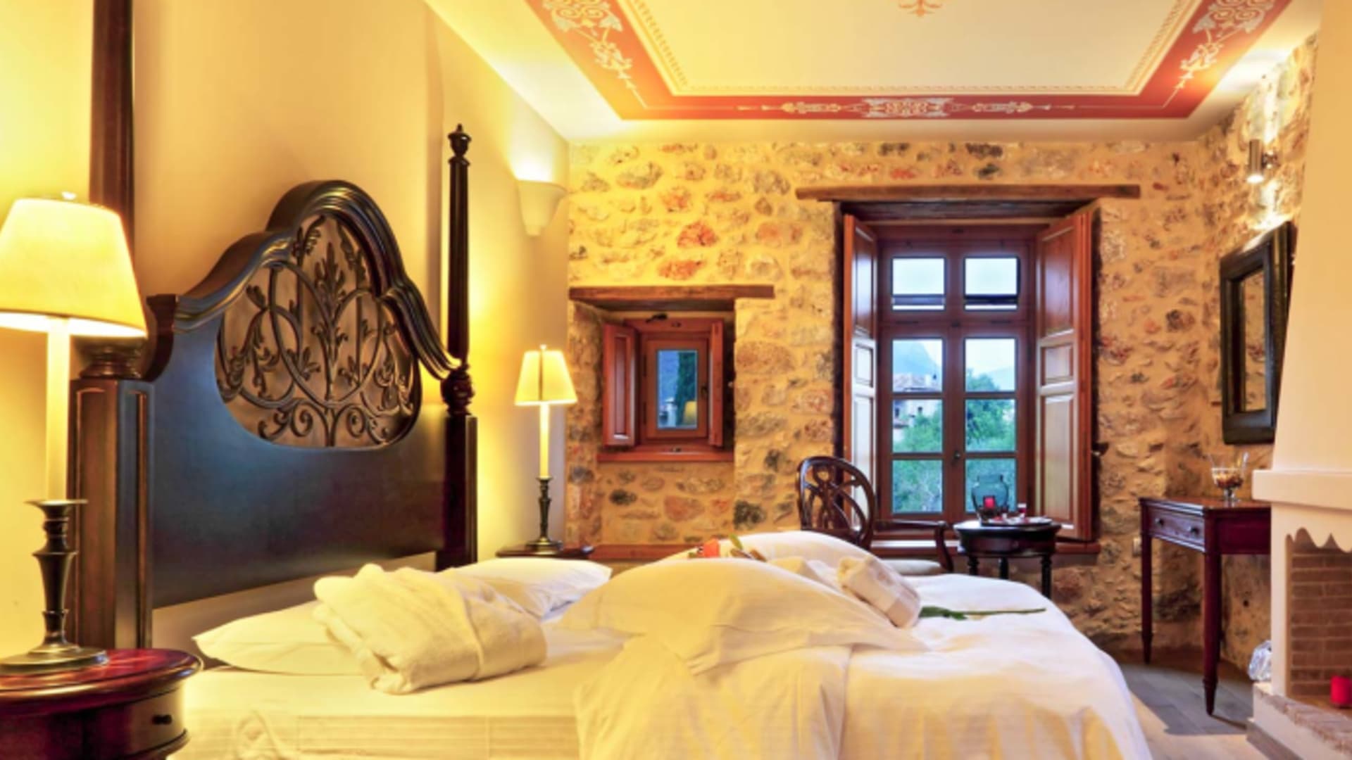 Doppelzimmer im Archontiko Chioti Boutique Hotel mit geschnitztem Holzkopfteil und mediterraner Natursteinwand.