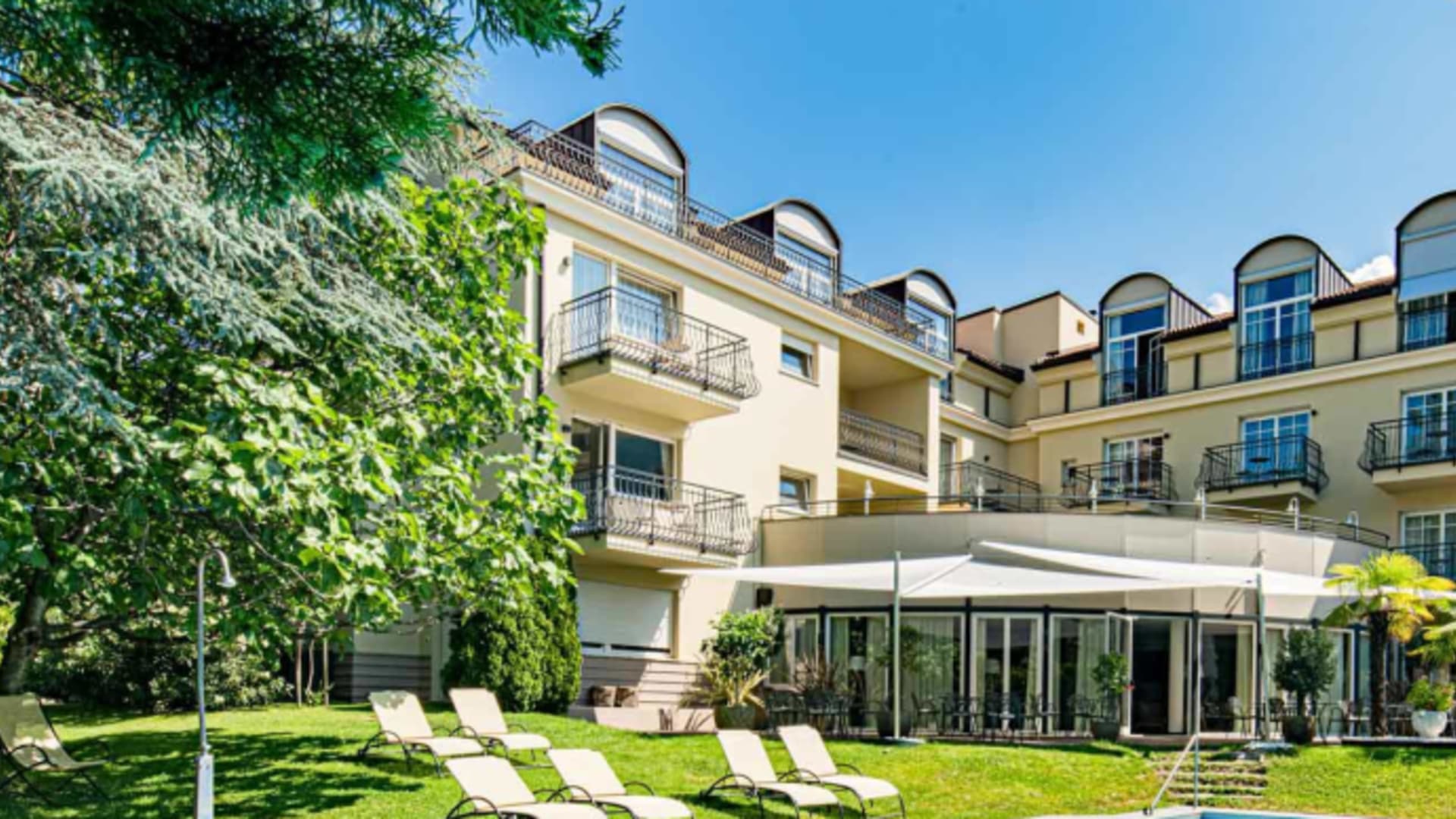 Außenansicht des Hotel Villa Laurus in Meran mit Swimming Pool und Terrasse vor bewaldeten Bergen.