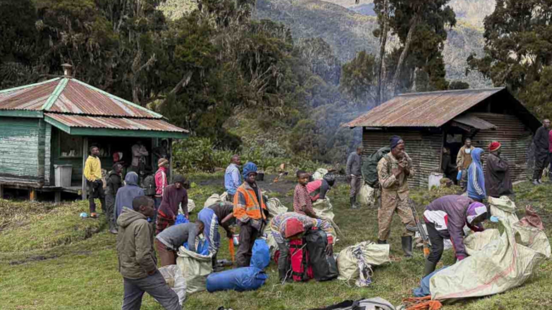 Camp-Organisation an der Berghütte im Rwenzori Gebirge Uganda mit Gepäcksäcken und Trägern vor Holzhütten.