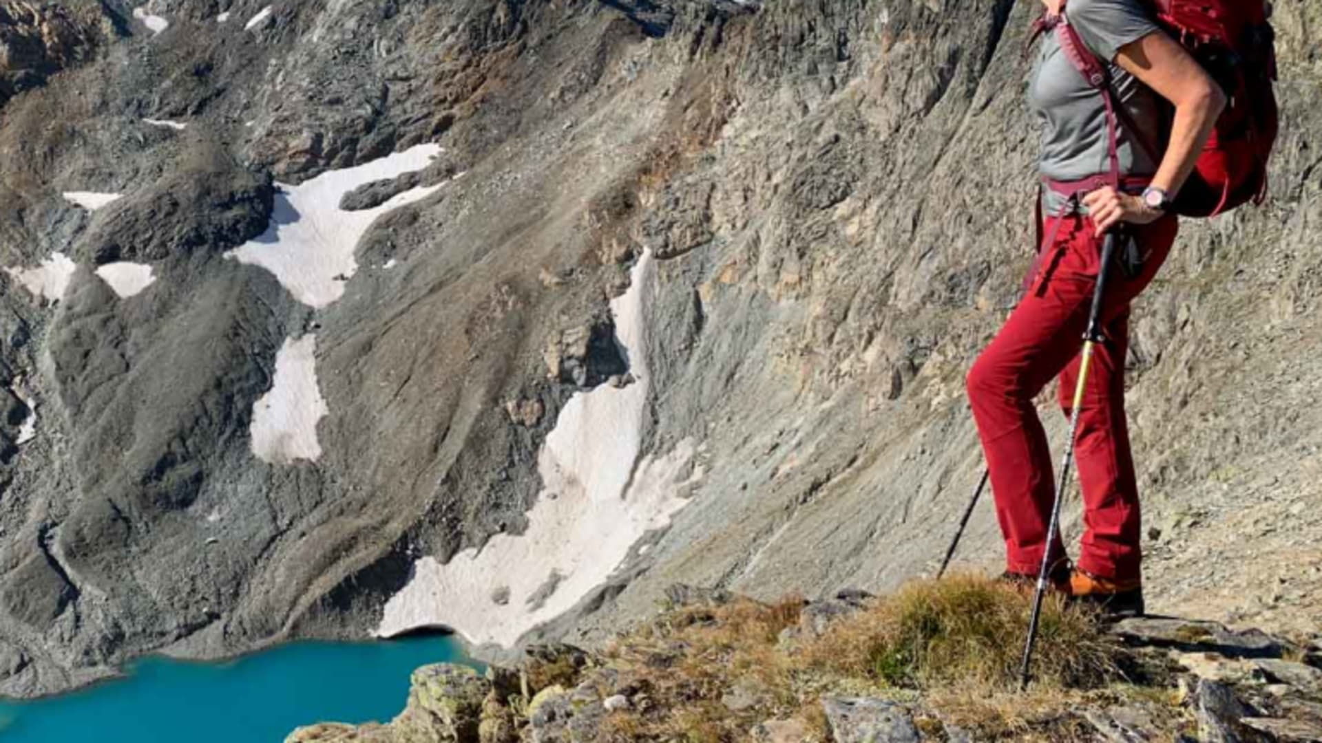 Bergwanderin mit rotem Rucksack auf Felsvorsprung blickt auf türkisfarbenen Gletschersee in der Verwallgruppe.