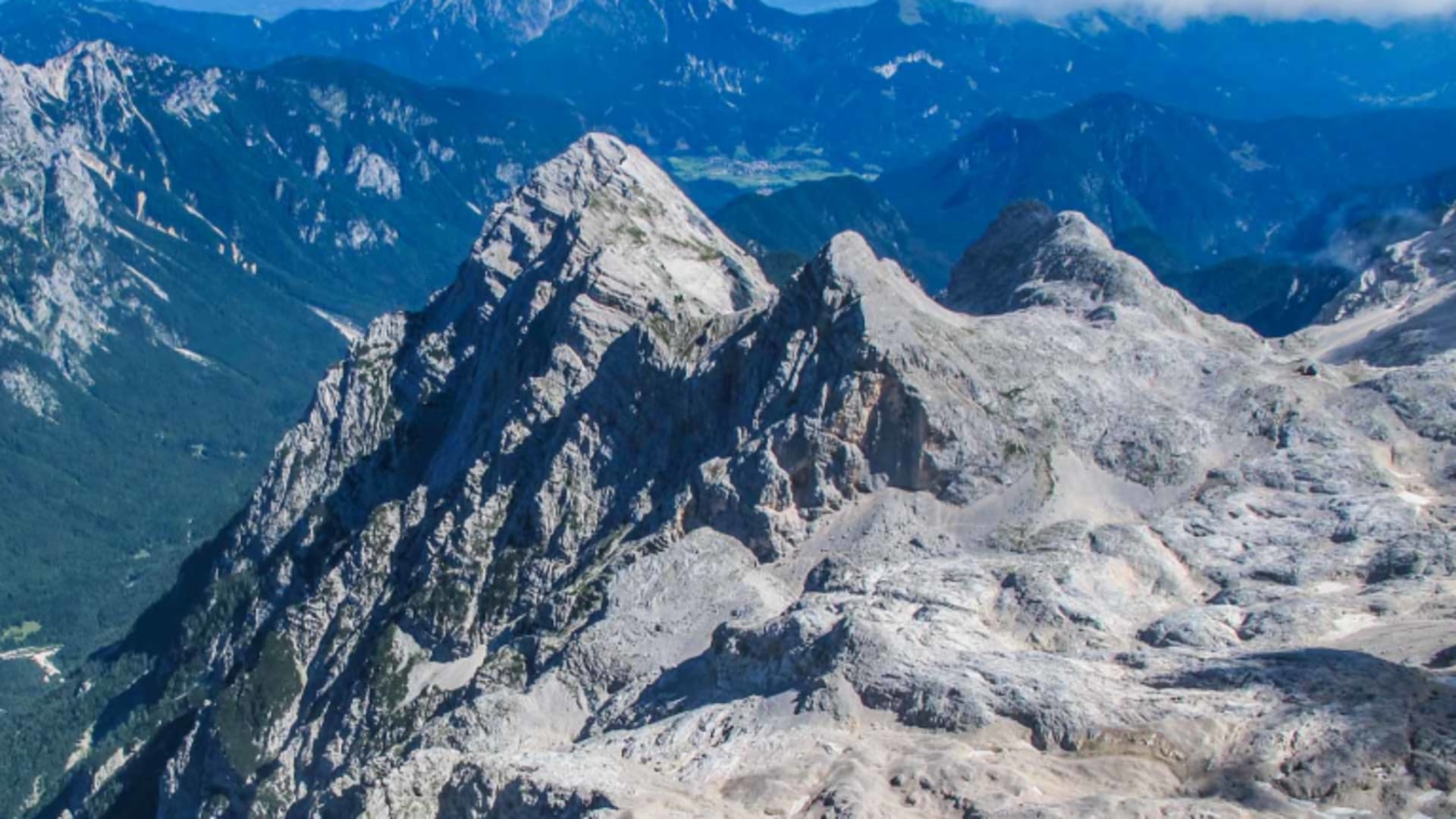 Bergwanderung in den Julischen Alpen: Weitwinkelpanorama mit Kalkfelsgrat, bewaldeten Tälern und gestaffelten Bergketten.