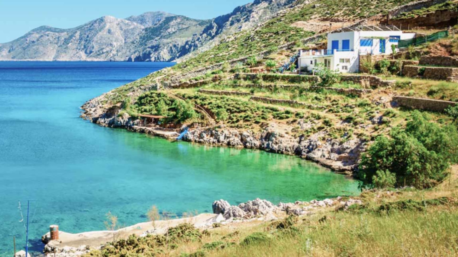 Klettern auf Kalymnos: Panoramablick auf türkisfarbene Meeresbucht mit felsigen Hängen, weißem Gebäude mit blauen Fensterläden