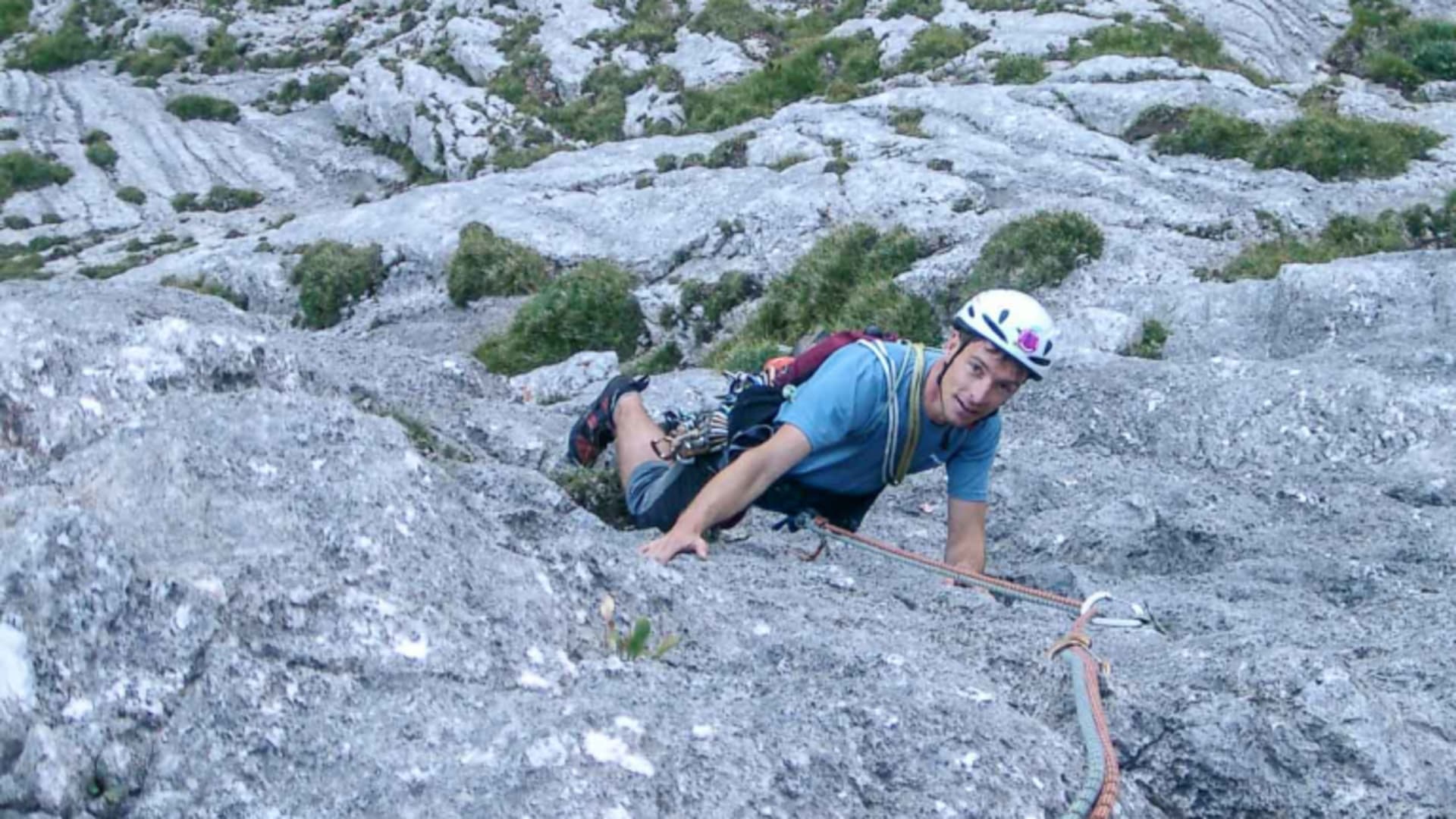Kletterer mit weißem Helm und Rucksack steigt an geneigter Kalksteinplatte in den Allgäuer Alpen auf, Seil am Haken.