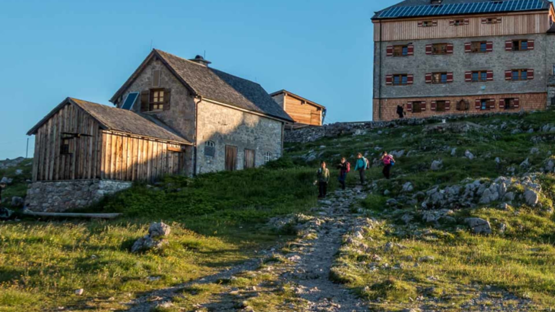 Vier Bergsteiger mit Rucksäcken steigen auf dem Schotterweg zum Watzmannhaus auf, dem Stützpunkt für Klettern
