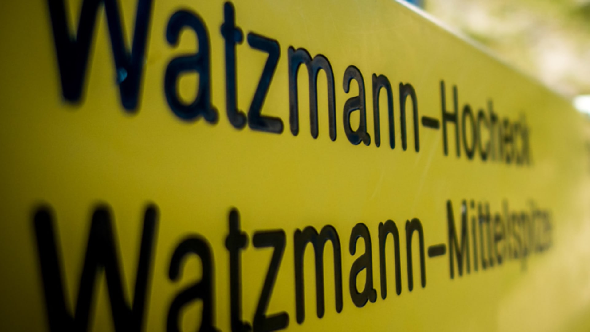 Gelbes Wegweiserschild am Watzmann mit Einträgen zu Watzmann-Hocheck und Watzmann-Mittelspitze bei blauem Himmel.