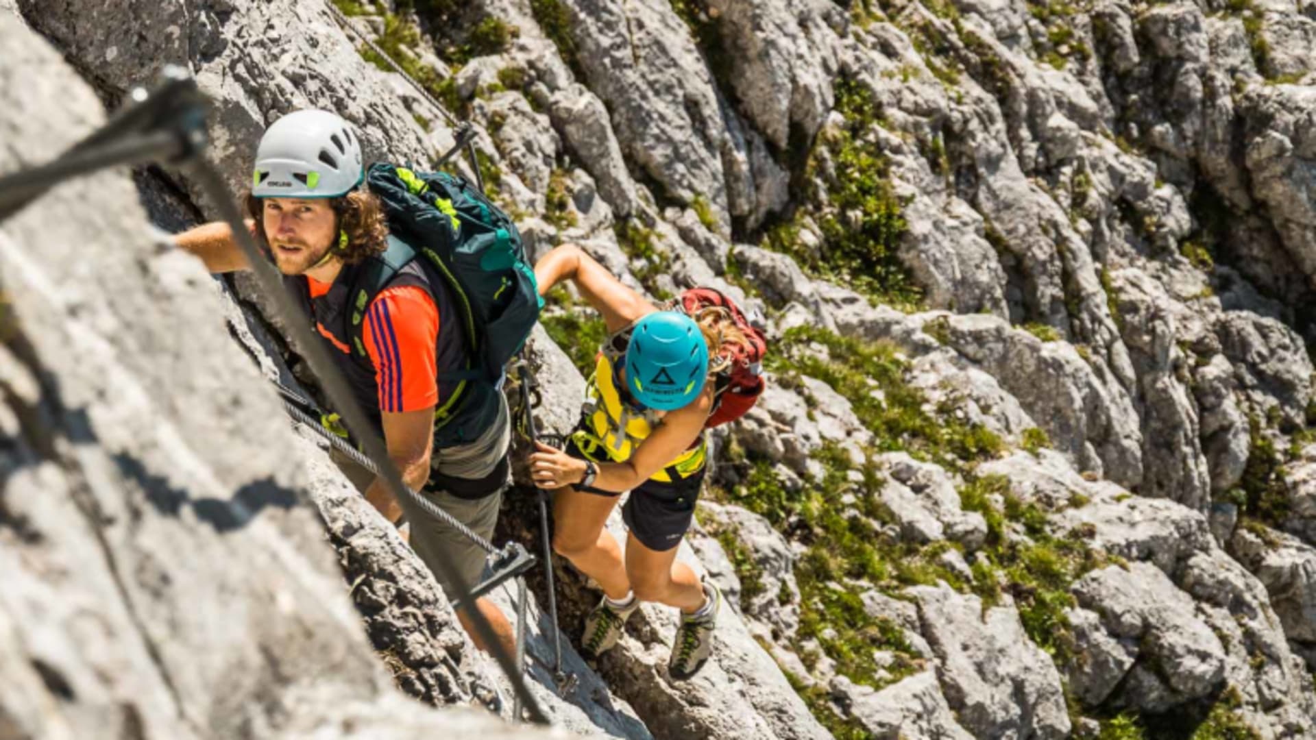 Drei Personen steigen beim Klettersteig an einer gesicherten Kalkfelswand in den Berchtesgadener Alpen auf.